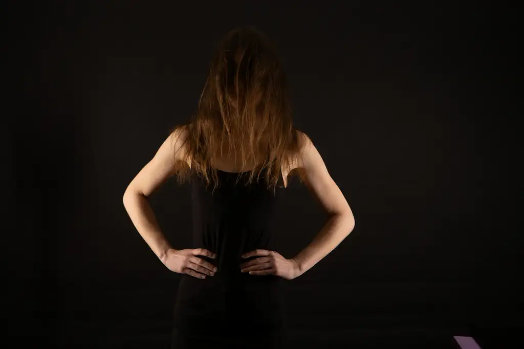 Žena stoji sa rukama na bokovima ispred tamne pozadine